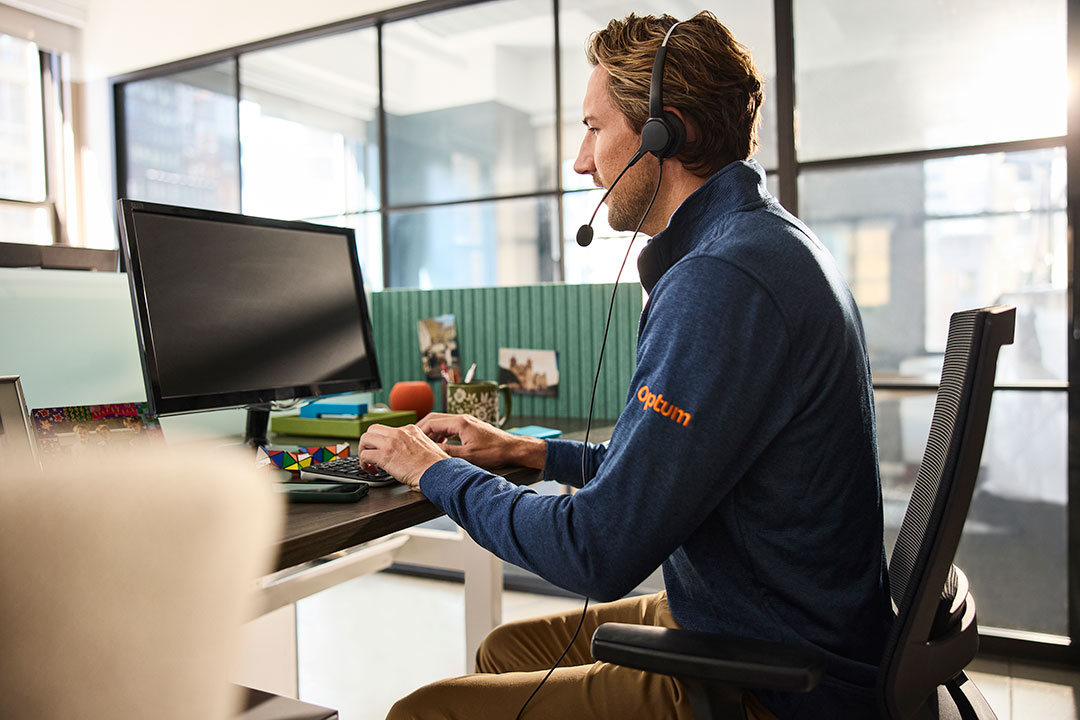Person wearing a headset works at a desk with a computer in a modern office.