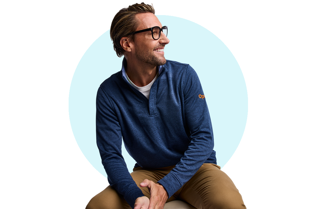 Seated person wearing a blue long‑sleeve top and glasses against a light background.