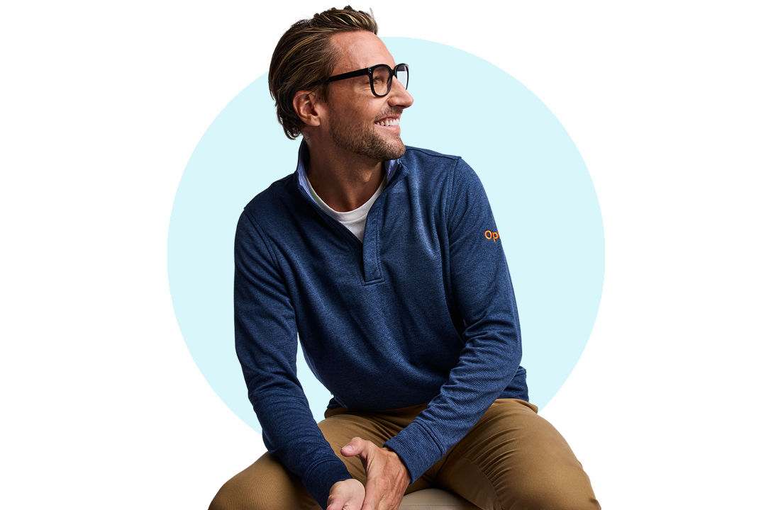 Seated person wearing a blue long‑sleeve top and glasses against a light background.